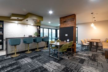 a lounge area with tables and chairs and a bar with stools at 310 at Nulu Apartments-Student, Louisville, KY 40202
